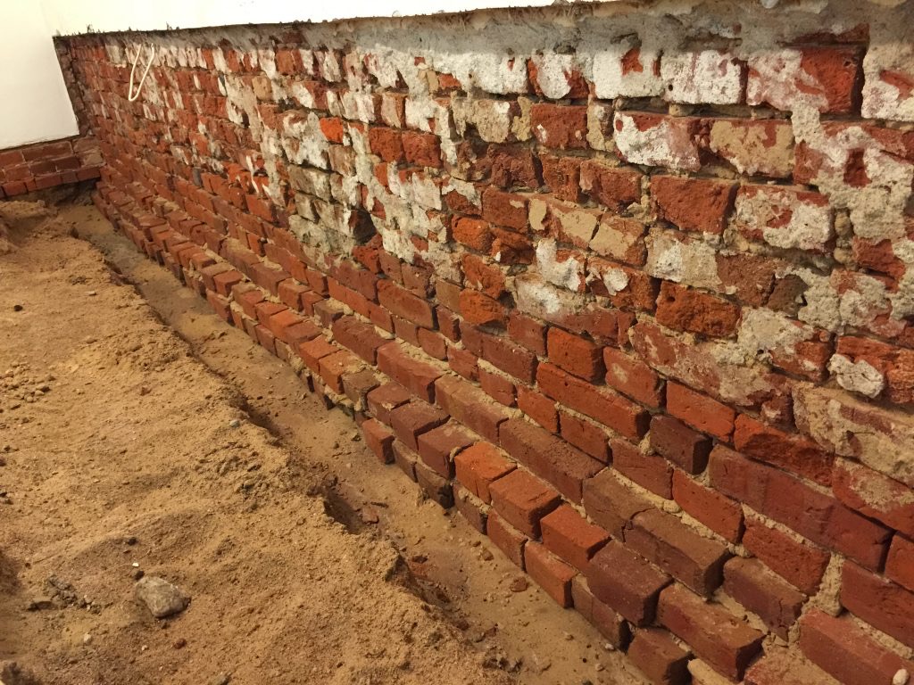 Auf dem Bild ist ein stark durchfeuchteter Keller mit geschädigtem Mauerwerk im unteren Wandbereich zu sehen. Sichtbar sind Feuchtigkeit, beschädigte Fugen und frühere Sanierungsbereiche. Solche Schäden zeigen, warum bei einer Kellerabdichtung nicht oberflächlich gearbeitet werden darf, sondern Ursache, Wandaufbau und Feuchtigkeitsverlauf fachgerecht beurteilt werden müssen.